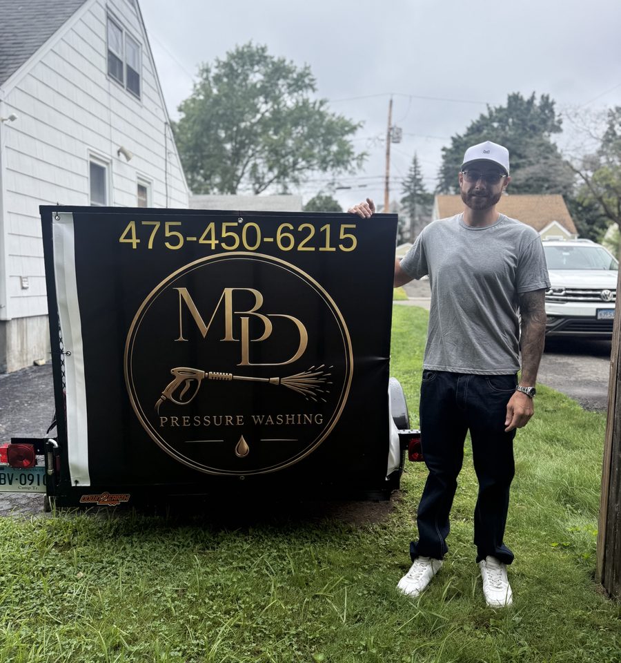 Matt, the owner of MBD Pressure Washing, standing beside the company trailer, which carries the gold MBD Pressure Washing logo and the phone number 475-450-6215.
